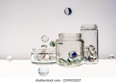 Glass Jars With Marbles Inside Or Falling Into The Jars, White Background