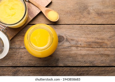 Glass jars and spoon of Ghee butter on wooden table, flat lay. Space for text