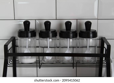 Glass Jars Stand In Row On Black Steel Shelf.