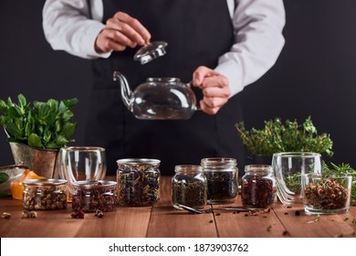 Glass Jars With Various Sorts Of Tea, Herbs And Tea Master Preparing A Pot. Barista Ready To Brew Perfect Blend Of Tea For Customers.