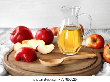 Glass jug with apple vinegar and fresh fruit on wooden board