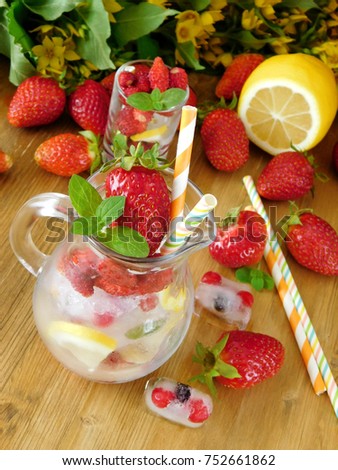 Glass jug full of ice cubes, berries, lemon slices and mint is prepared to be filled with a drink on a wooden background