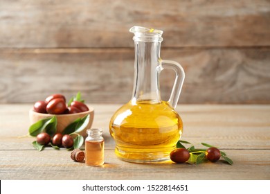 Glass jug with jojoba oil and seeds on wooden table