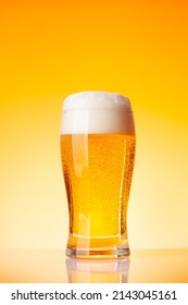 Glass with lager beer in front of yellow background. Studio shot