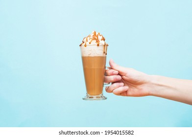 A glass of latte to hold in hand on a blue background. Serving coffee with milk, whipped cream and caramel - Powered by Shutterstock