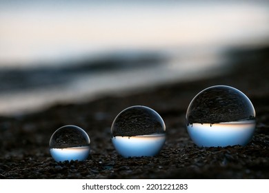 Glass Lens Globes On Sandy Beach On Sea Background At Sunset. Beauty, Fancy, Family, Evolution, Increase And Growth, Rise And Increment Concept