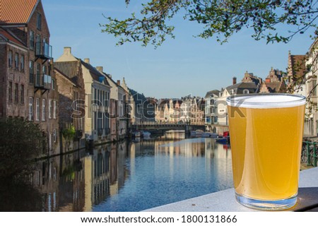 Glass of light beer against canal and historic buildings in Ghent, Belgium