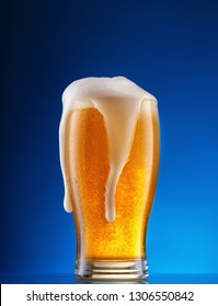 Glass Of Light Beer With Drip Foam On A Blue Background