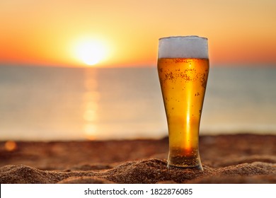 Glass Of Light Beer With Froth And Bubbles On The Sea Beach At Sunset