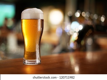 Glass of light beer on a dark pub.