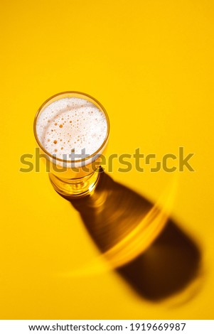 Glass of light beer on a yellow background, top view. Shadow from a glass of lager. 