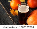 A glass of light beer pumpkin ale on a wooden table. Orange pumpkins and autumn leaves