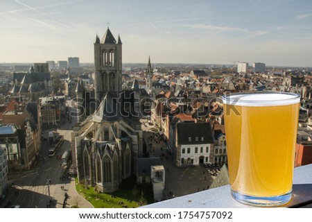 Glass of light Belgian beer against view of big cathedral in Ghent, Belgium. View from above of Ghent, Belgium