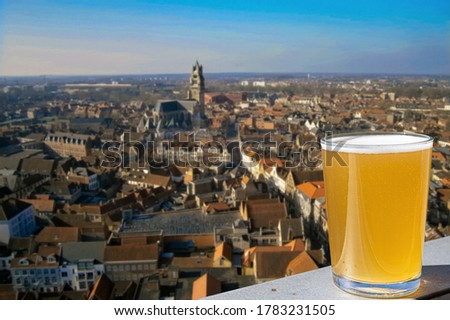 Glass of light Belgian beer with panoramic view from above of old town and big cathedral in Ghent, Belgium. View from above of Ghent, Belgium