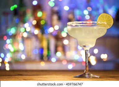 Glass of margarita cocktail on bar lights background.