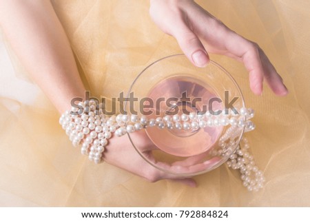A glass for a martini. Pink alcoholic cocktail. A woman's tender mood. Pearl beads in a gold fabric and on a hand.