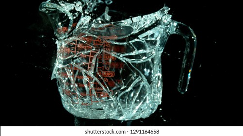 A Glass Measuring Cup Shattering, breaking, exploding into shards on black. Glass begins separating. 