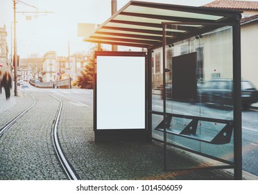 Glass and metal tram stop with railway track near and blank white mock-up of informational banner inside; empty advertising billboard placeholder stand in urban settings next to tramway and city road