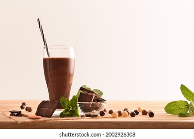 Glass With Milk Chocolate Shake On Wooden Table With Portions Of Chocolate And Mint Leaves With Isolated Background