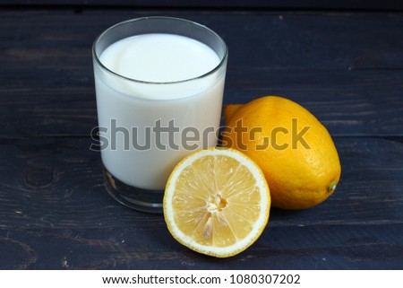 A glass of milk and lemons on a dark wooden background