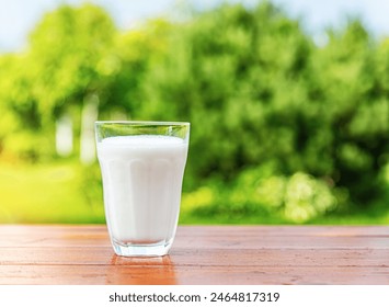 A glass of milk on a wooden table against the backdrop of a summer garden. - Powered by Shutterstock