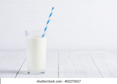 Glass of milk with paper striped straw on white wooden table still life with copy space