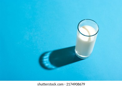 Glass of milk under the bright light with hard shadow on blue backgorund. - Powered by Shutterstock