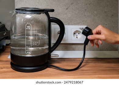 glass modern electric kettle stands on the table against the background of an outlet. Boiling water. Electricity consumption by household electrical appliances - Powered by Shutterstock