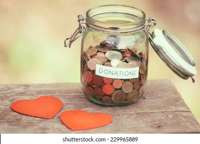 Glass Money Jar With A Label With The Word Donations On It And Two Handcrafted Wooden Heart Shapes.