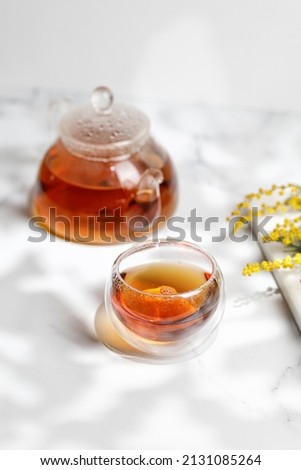 A glass mug or cup with herbal tea and a teapot in sunny day. Spring, summer.