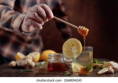 Glass mug of ginger tea with honey , lemon and mint on old wooden table .Man puts a honey in a Cup of tea.  Selective focus . - Powered by Shutterstock