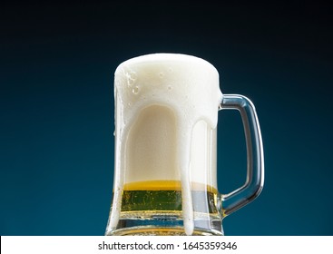 Glass mug overflowing with fresh foamy beer pouring over the edge