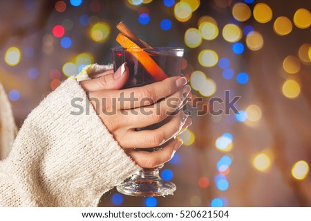 Glass with mulled wine in the hands of a girl on the background of Christmas lights