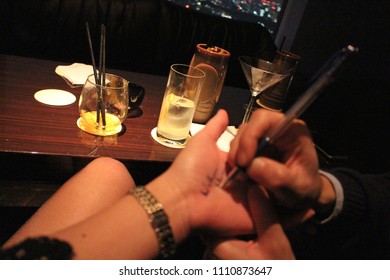 Glass Of A Night Out Behind Blur Hand Of Man Writing Phone Number On Woman Hand