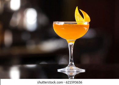 Glass of orange cocktail decorated with lemon at bar counter background.
