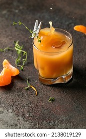 Glass with orange juice or alcohol with ice, thyme and mandarin slice. Dark background, bursts, drops. For the menu of a bar, restaurant, cafe. Close up.