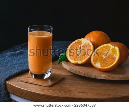 A glass of orange juice standing next to fresh oranges placed on a round wooden tray. The photo is styled in dark food style. Perfect for use in diet catalogs, culinary books, and health food blogs.