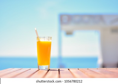 A glass of orange juice stands on a wooden table. Cocktail on the background of the blue sea. Vacation, vacation, summer, pleasure concept.