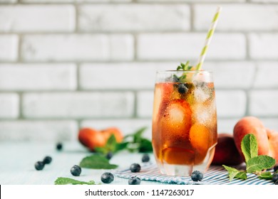 The glass of peach ice tea on wooden table. Cuba Libre or long island iced tea cocktail, cold drink or lemonade with fruits and mint, bilberry, blueberry - Powered by Shutterstock