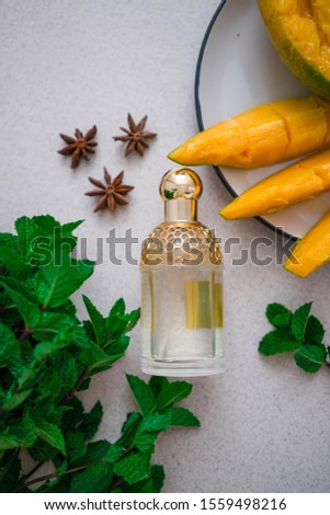 
glass perfume bottle with a bunch of mint, slices of fresh mango and anise stars