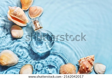 Glass perfume bottle and sea shells in spray water background. Marine summer fragrance concept