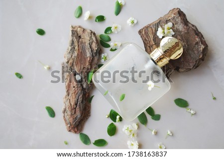 
glass perfume bottle with small white  flowers, leaves and fragments of wooden bark. A concept of fresh wood unisex aroma