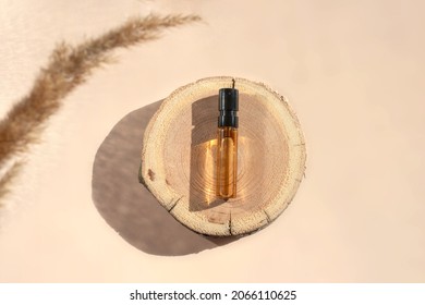 Glass Perfume Sample With Transparent Brown Liquid On A Wooden Tray Lying On A Beige Background With Pampas Grass. Luxury And Natural Cosmetics Presentation. Tester On Woodcut In Sunlight. Top View