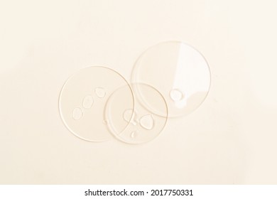 Glass-Petrischale mit transparentem reinem Serum für Hautpflege auf beigem Hintergrund, Draufsicht. Konzeption von Labortests und Forschung