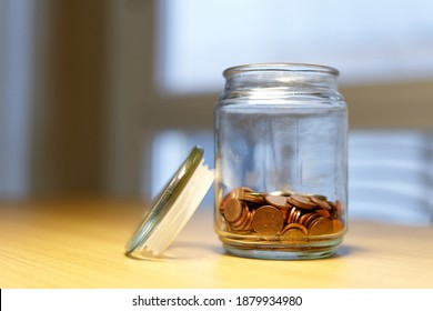 glass piggy bank spilling coins on wooden table. glass jar with euro coins and golden lid. coins scattered around the table. open piggy bank with coins coming out - Powered by Shutterstock