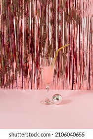 A Glass Of  Pink Drink With Disco Ball Against Shiny Rose Gold Tassles.