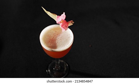 A Glass Of Pink Frothy Drink With Petals On A Black Background