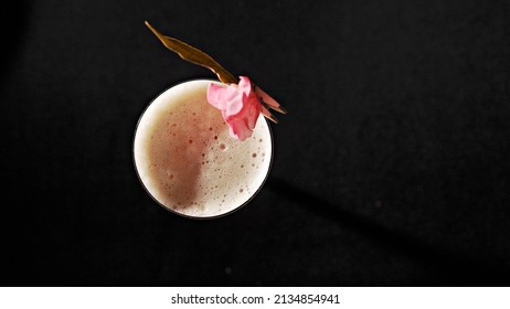 A Glass Of Pink Frothy Drink With Petals On A Black Background