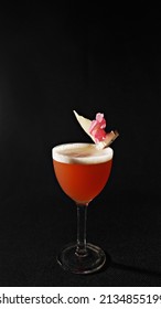 A Glass Of Pink Frothy Drink With Petals On A Black Background