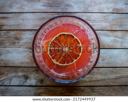 Glass of pink soda drink with ice on wooden background. Top view